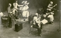 Five men standing on stage playing instruments